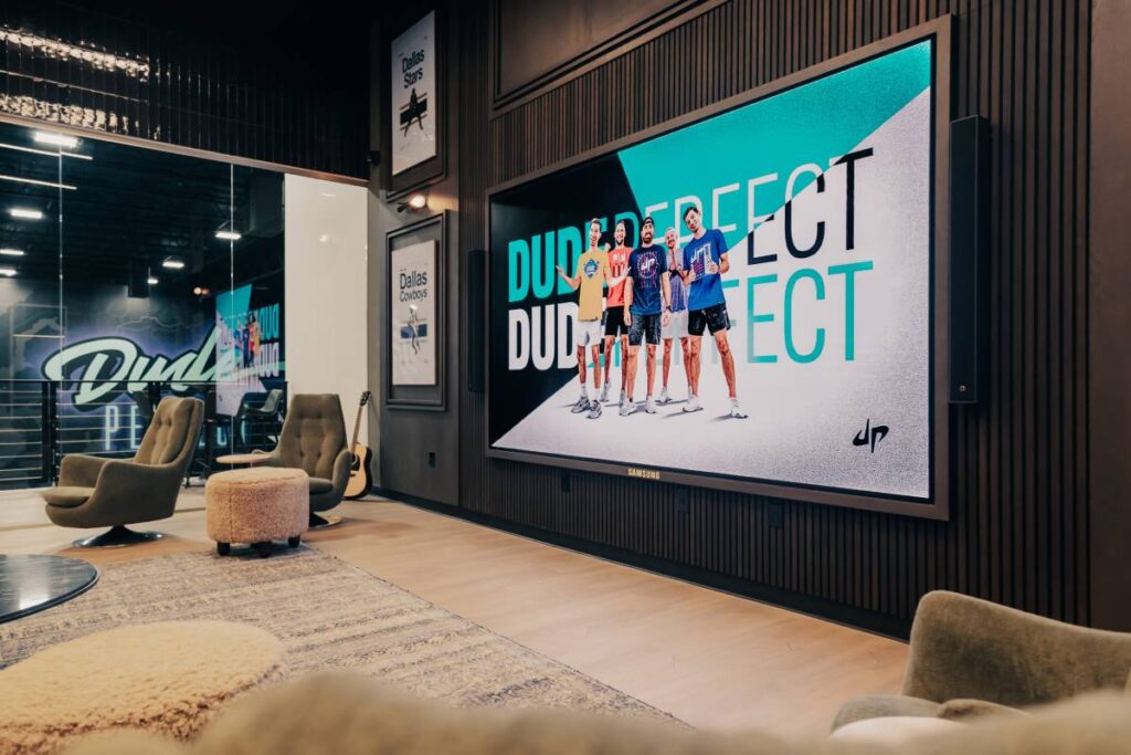 The giant Samsung LED display in Dude Perfect’s executive lounge is flanked by L-Acoustics Syva loudspeakers, wall-mounted along the left and right edges
